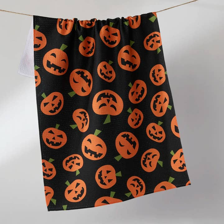 Black waffle weave tea towel with an all-over orange jack-o'-lantern pattern hanging on a line.
