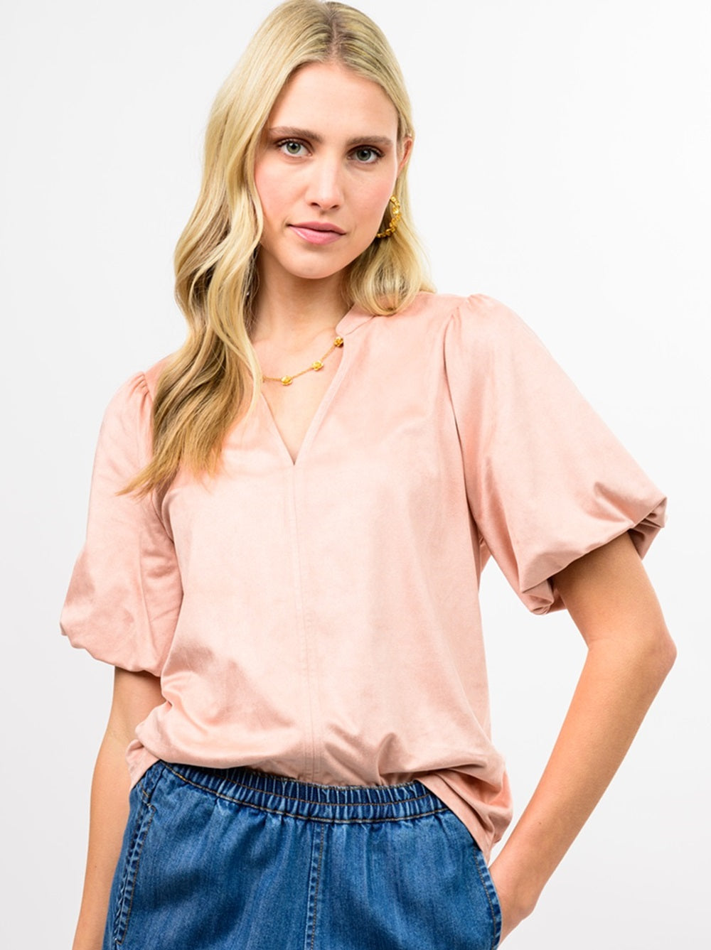Woman wearing a pink Sandy Faux Suede Poof Sleeve Top with a V-neckline and denim bottoms.