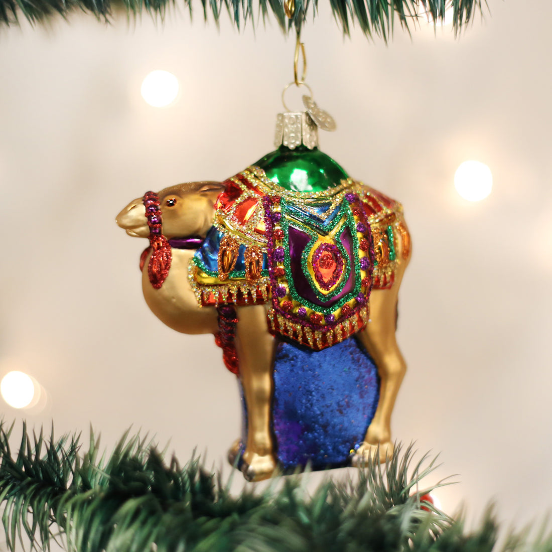 Magi's Camel glass ornament with colorful glittered saddle hanging on a Christmas tree branch.