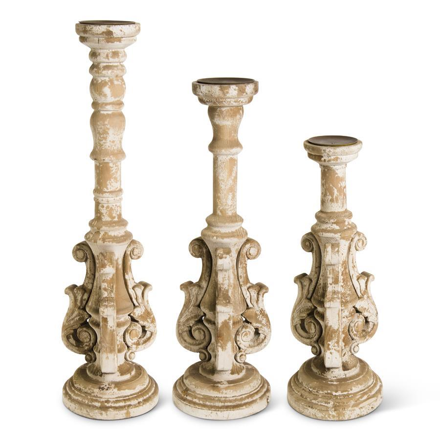 Three distressed wood ornate candleholders in varying heights with intricate sculptural details.