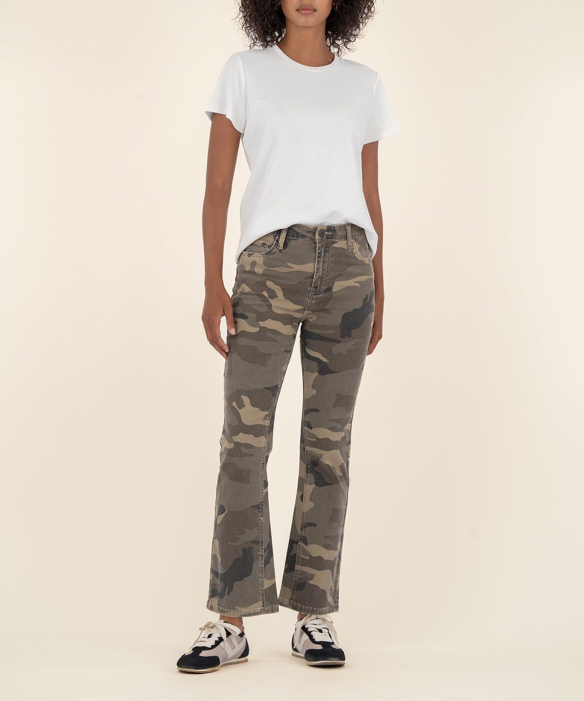 Woman wearing Kelsey high rise ankle flare pants in a camouflage print with a white t-shirt.