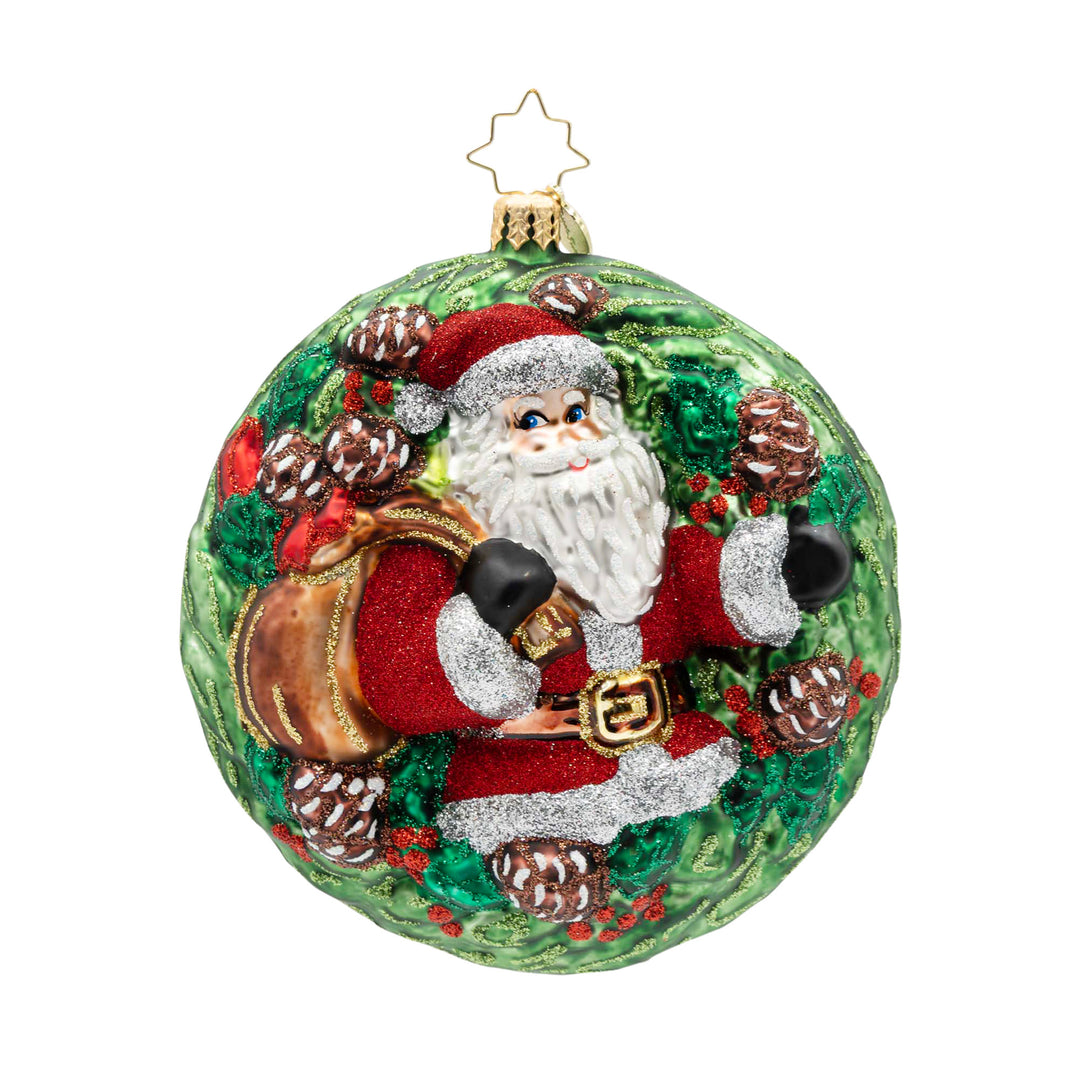 Round glass Christmas ornament featuring Santa Claus inside a green wreath with pinecones.