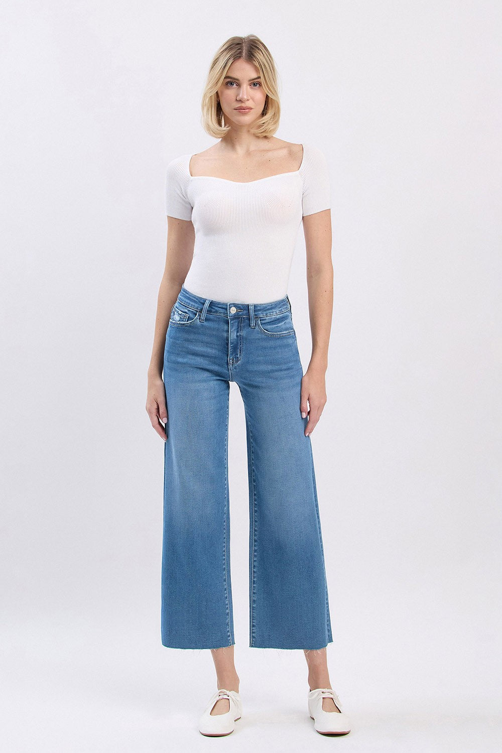 Woman wearing Audrey high rise slim wide leg cropped jeans with a raw hem and white ribbed top.