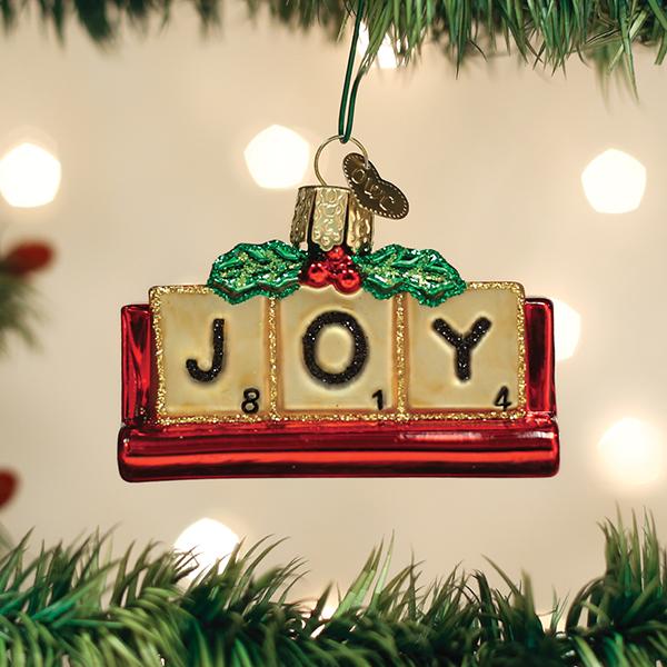 Red glass Joy ornament with gold glitter accents hanging on a Christmas tree branch.