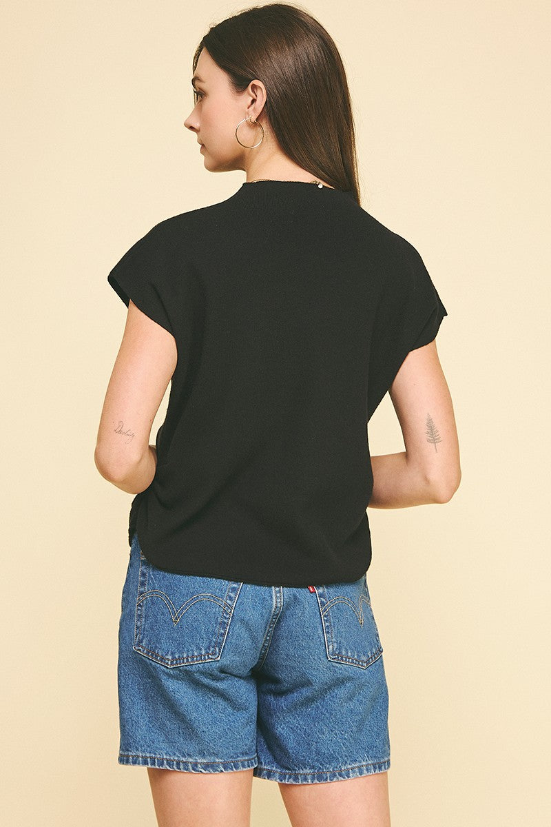 Back view of a woman wearing a black mock neck Chloe sweater vest with cap sleeves and blue shorts.