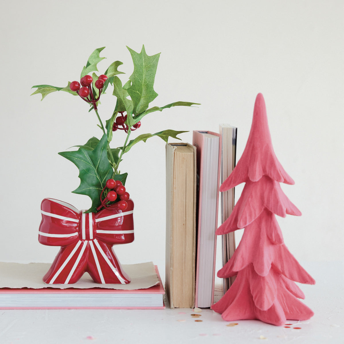 Red and white striped ceramic bow-shaped vase holding holly sprigs on a stack of books.