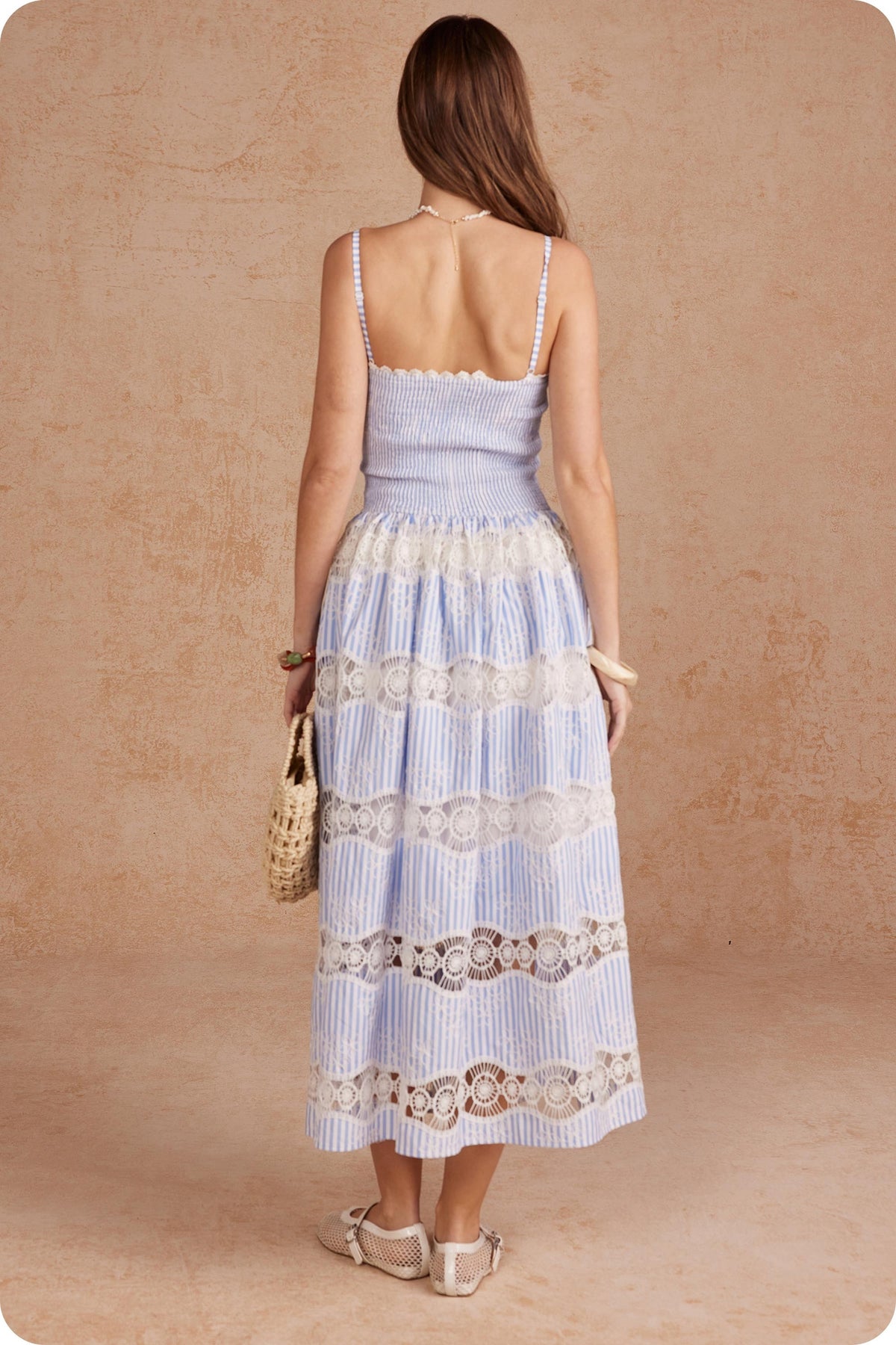 Back view of a woman in a blue and white striped sleeveless long dress with crochet lace inserts.