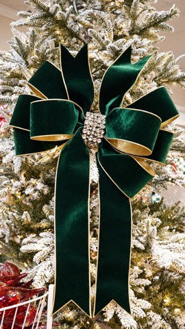 Emerald green velvet holiday bow with gold trim and a rhinestone center on a Christmas tree.