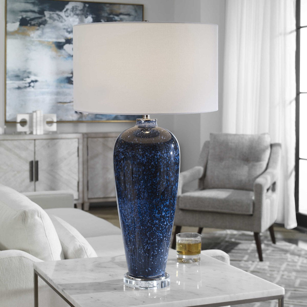 Stargazer Table Lamp with a blue speckled ceramic base and white drum shade on a marble table.