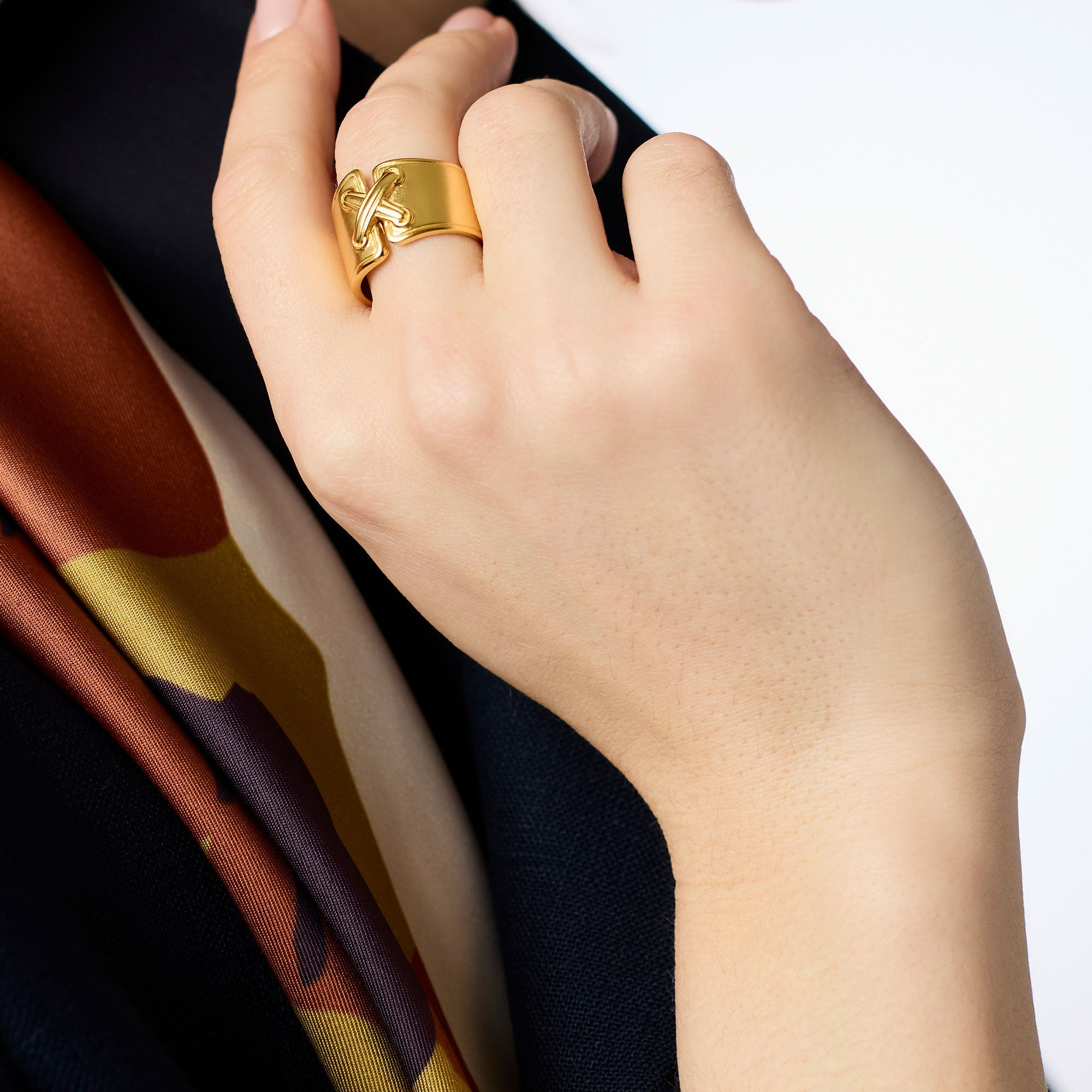 A person wearing the gold Essex Ring, featuring a wide band with a raised cross design.