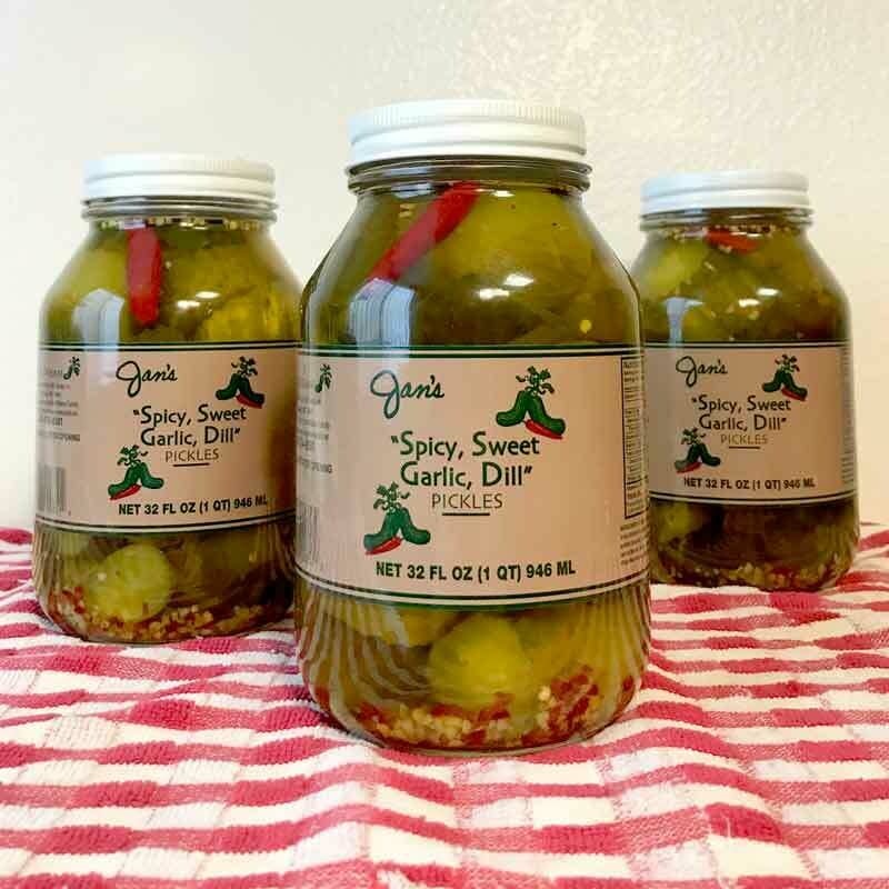 Glass jar containing Jan's Pickles spicy sweet garlic dill pickles with visible vegetables in brine.