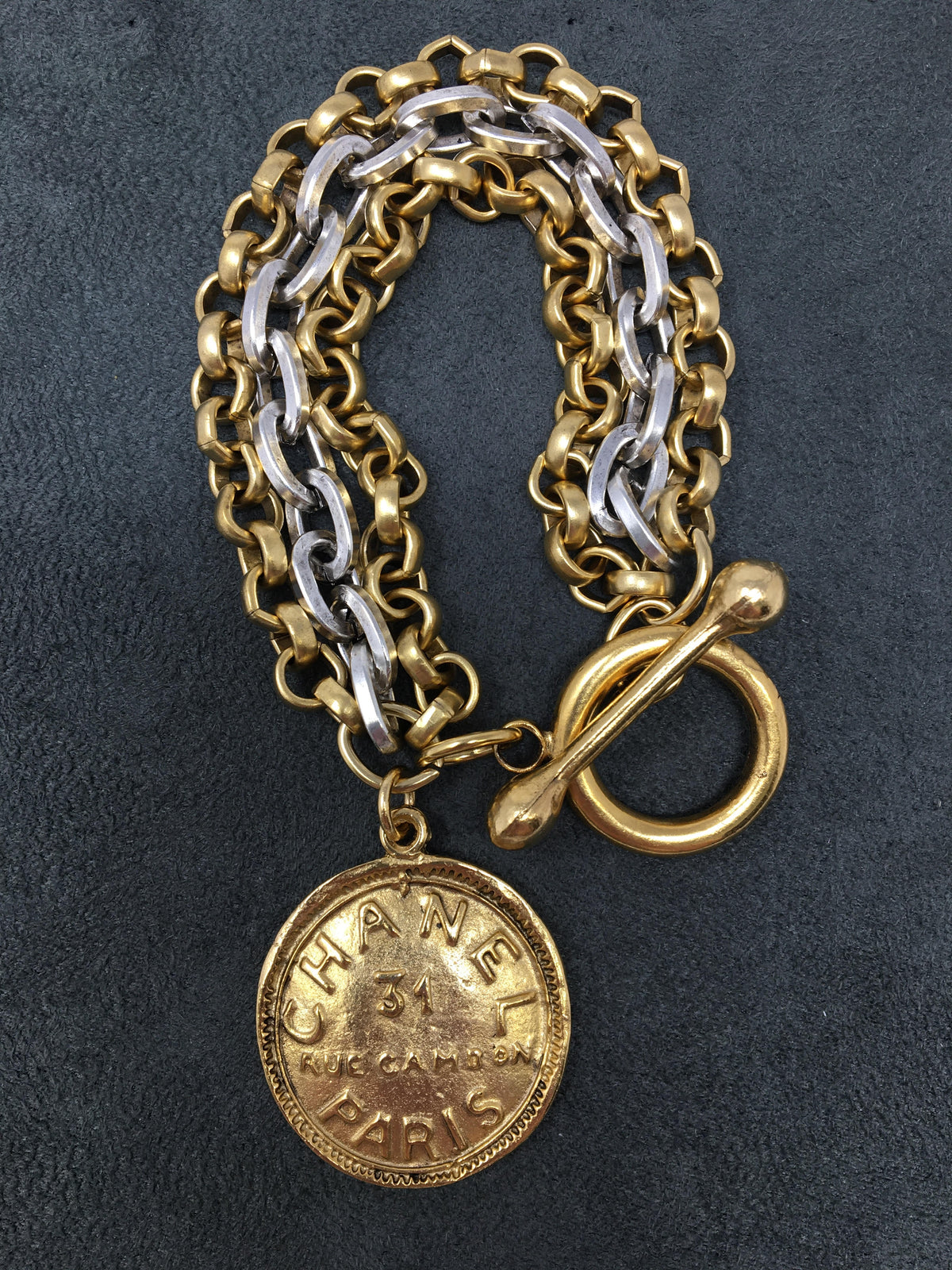 Triple strand bracelet in gold and silver chains with a toggle clasp featuring a Chanel-style coin charm.