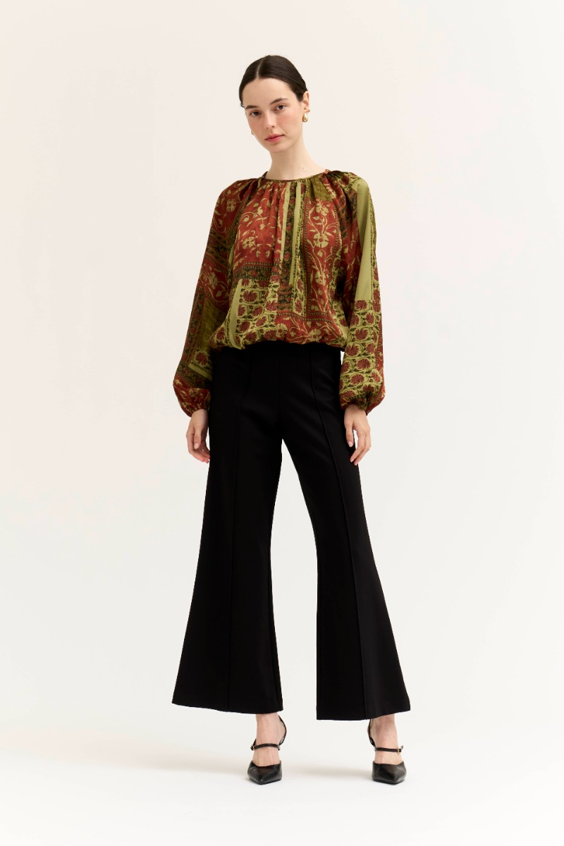 Woman wearing the Amy Printed Voluminous Top with vintage-inspired print and black flared trousers.