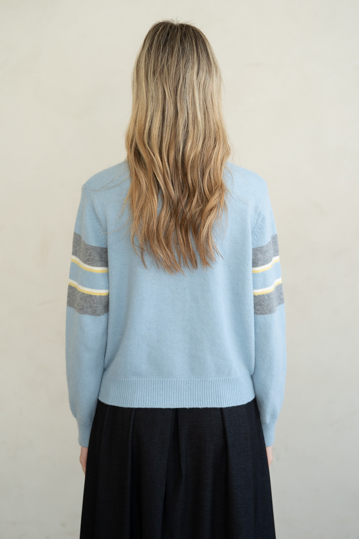 Back view of a light blue crew neck cardigan with grey and yellow stripes on the sleeves.