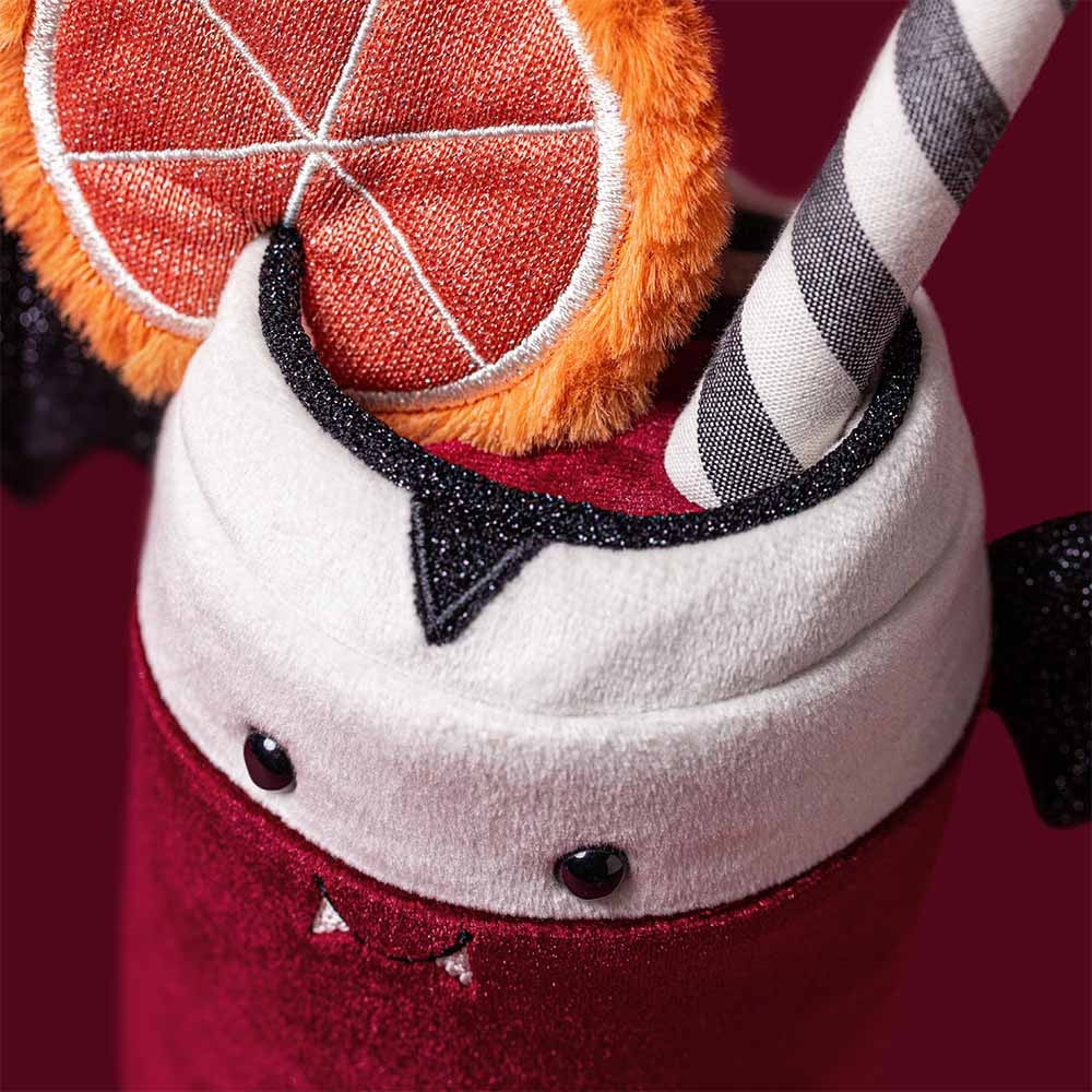 Close-up of a red plush drink with vampire fangs, a striped straw, and an orange slice garnish.