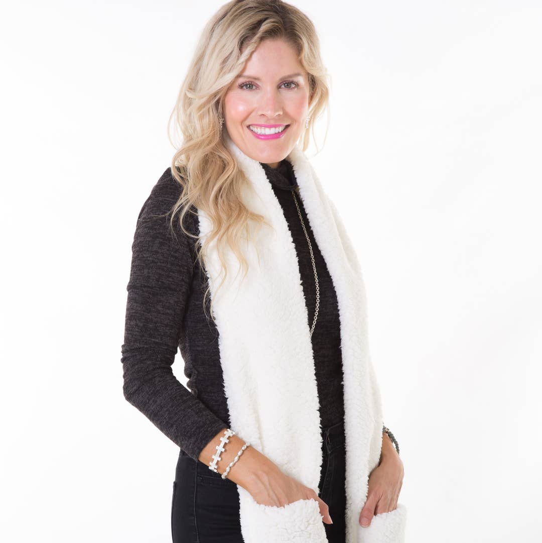 Woman wearing a white plush faux fur scarf with built-in pockets over a black long-sleeve top.