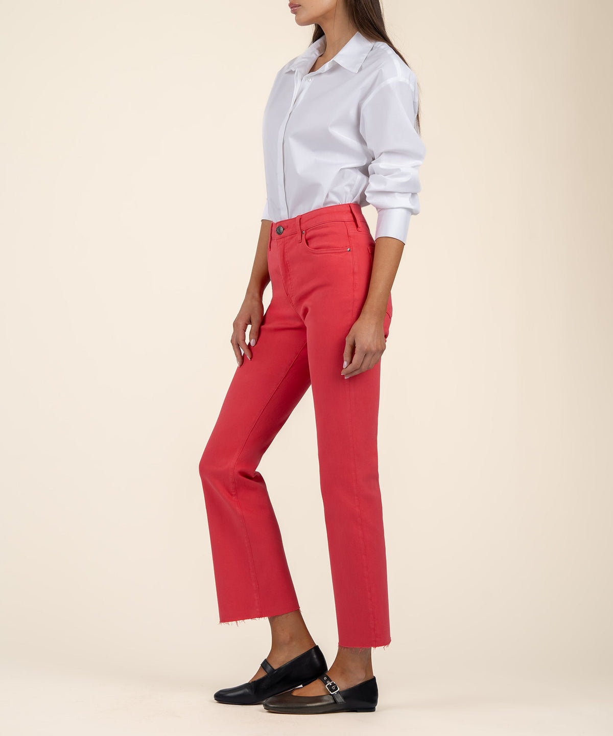 Woman wearing Kelsey high rise coral ankle flare jeans with a raw hem and a white button-down shirt.
