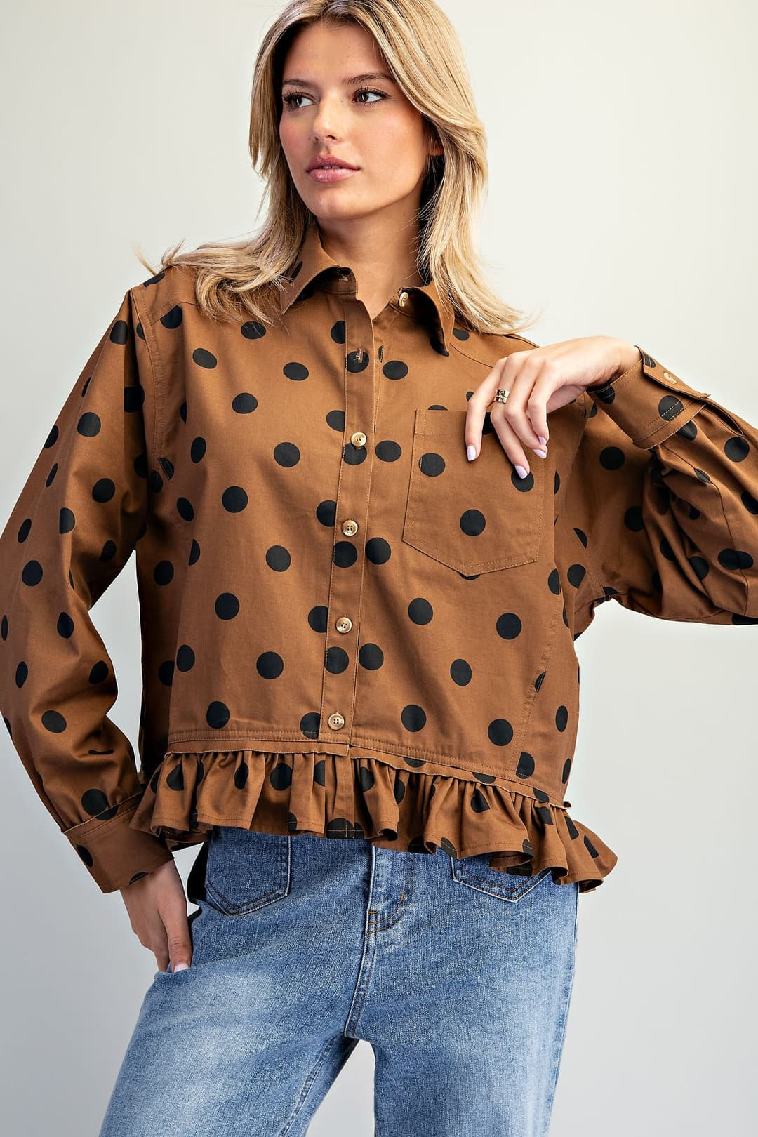 Clara brown button-down blouse with black polka dots, pointed collar, and ruffled hem.