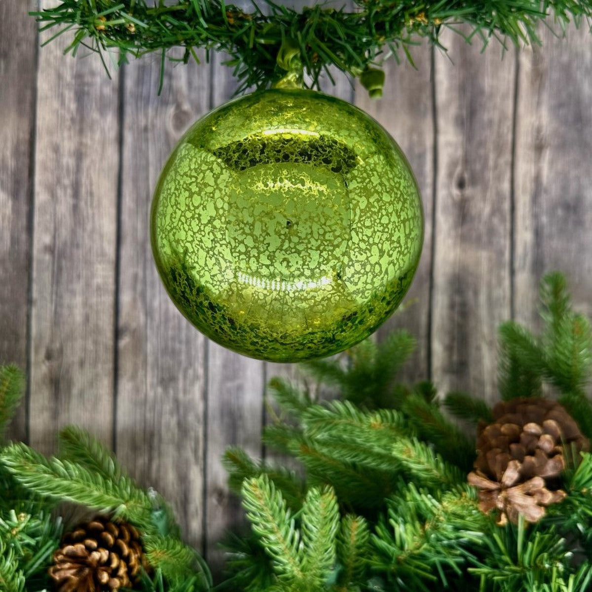 Hand-blown green mercury glass ornament with a vintage finish hanging from a pine branch.