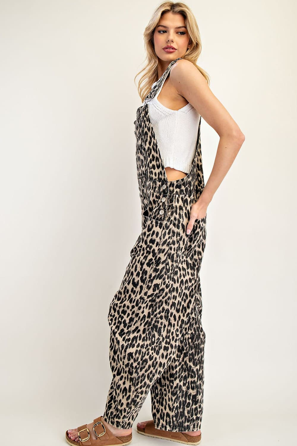 Woman wearing leopard print barrel leg overalls with a white tank top and brown sandals.