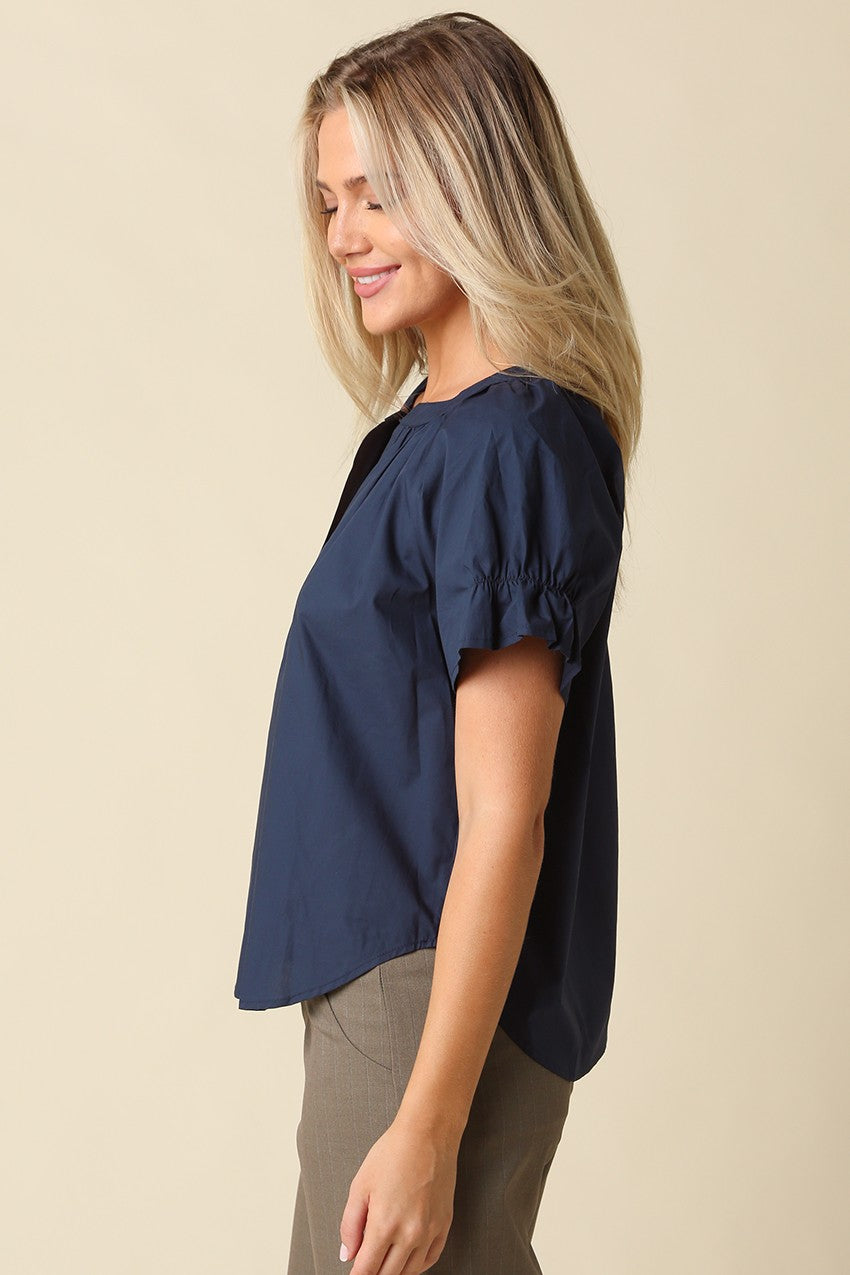 Side view of a woman wearing a navy blue Hylee Ruffle Sleeve Peasant Blouse with olive pants.