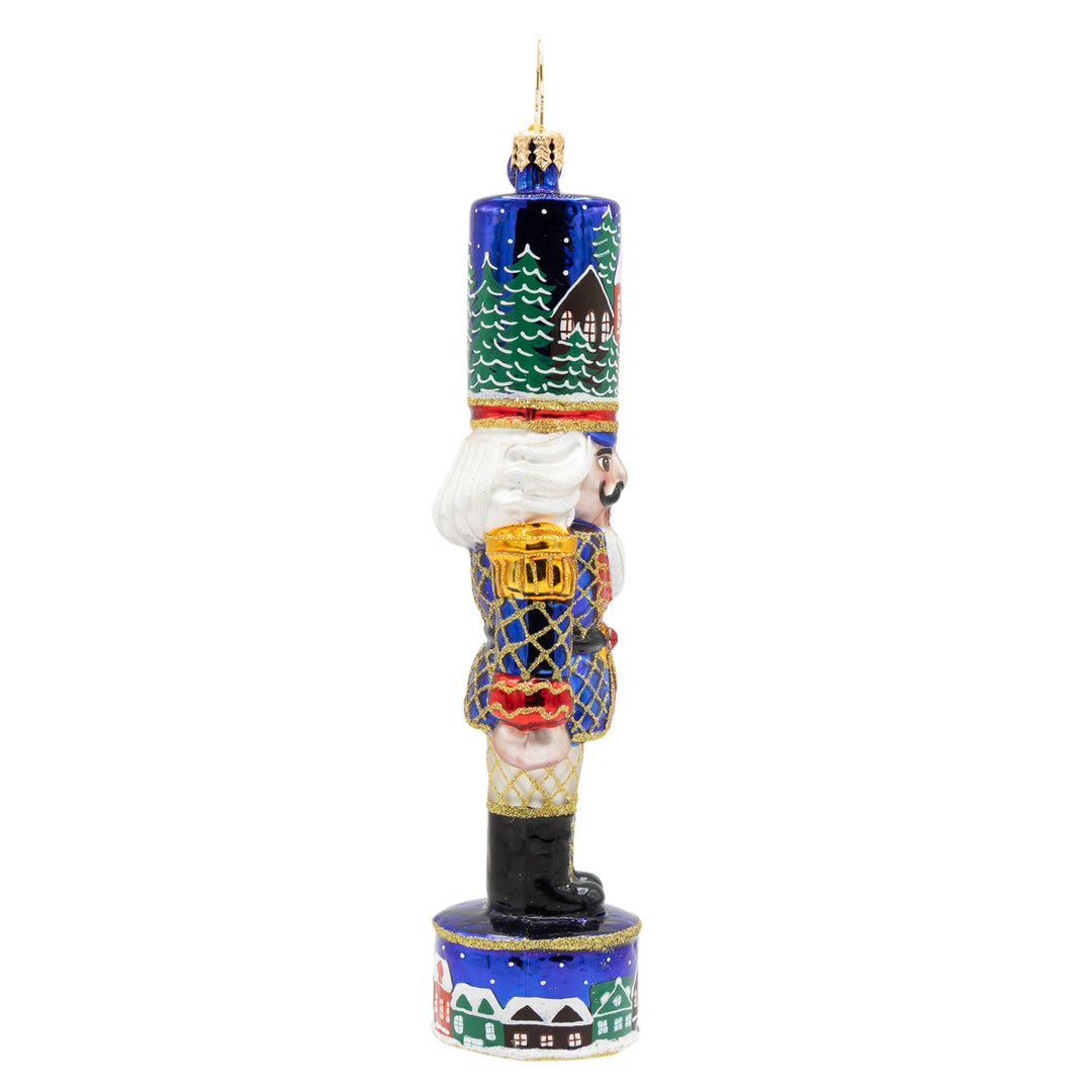 Christmas Sentinel nutcracker ornament in royal blue with snowy village scenes and gold glitter.