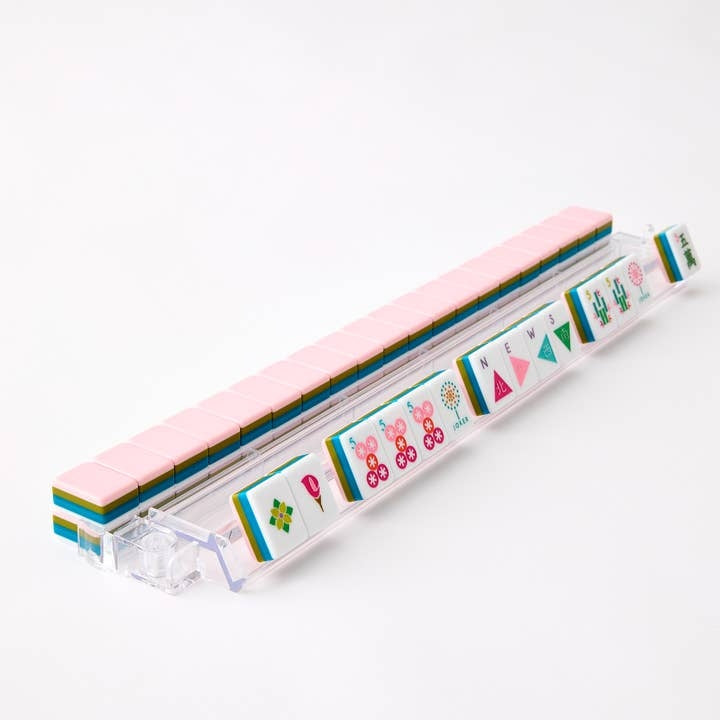 La Fete Mahjong tiles in pink, teal, and olive green on a clear acrylic rack.