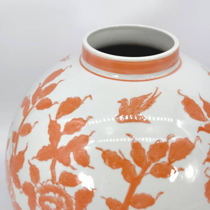 Close-up of a white ceramic globe vase with orange Chinoiserie floral and bird patterns.