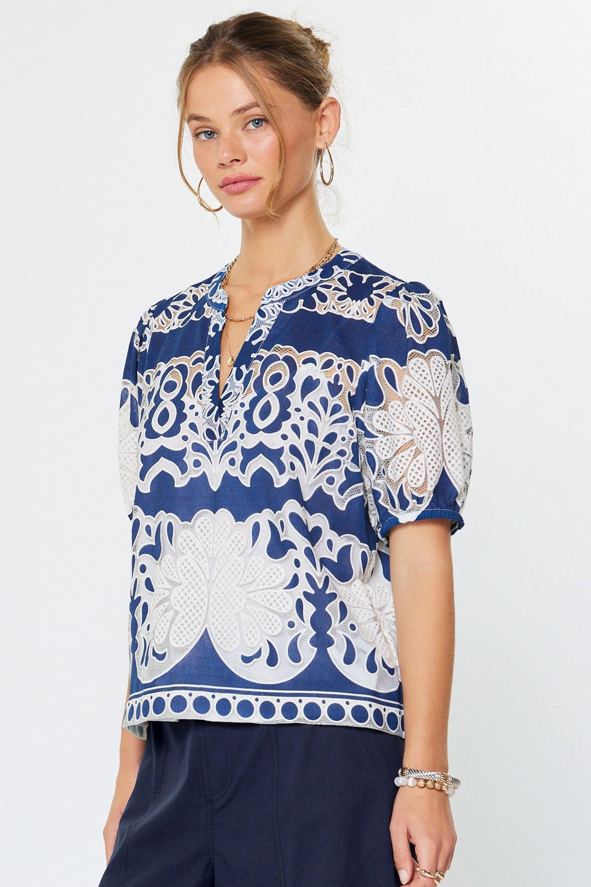 Relaxed fit rayon blouse with all-over lace embroidery floral medallions, split v-neckline, short puff sleeves, and inner cami lining.