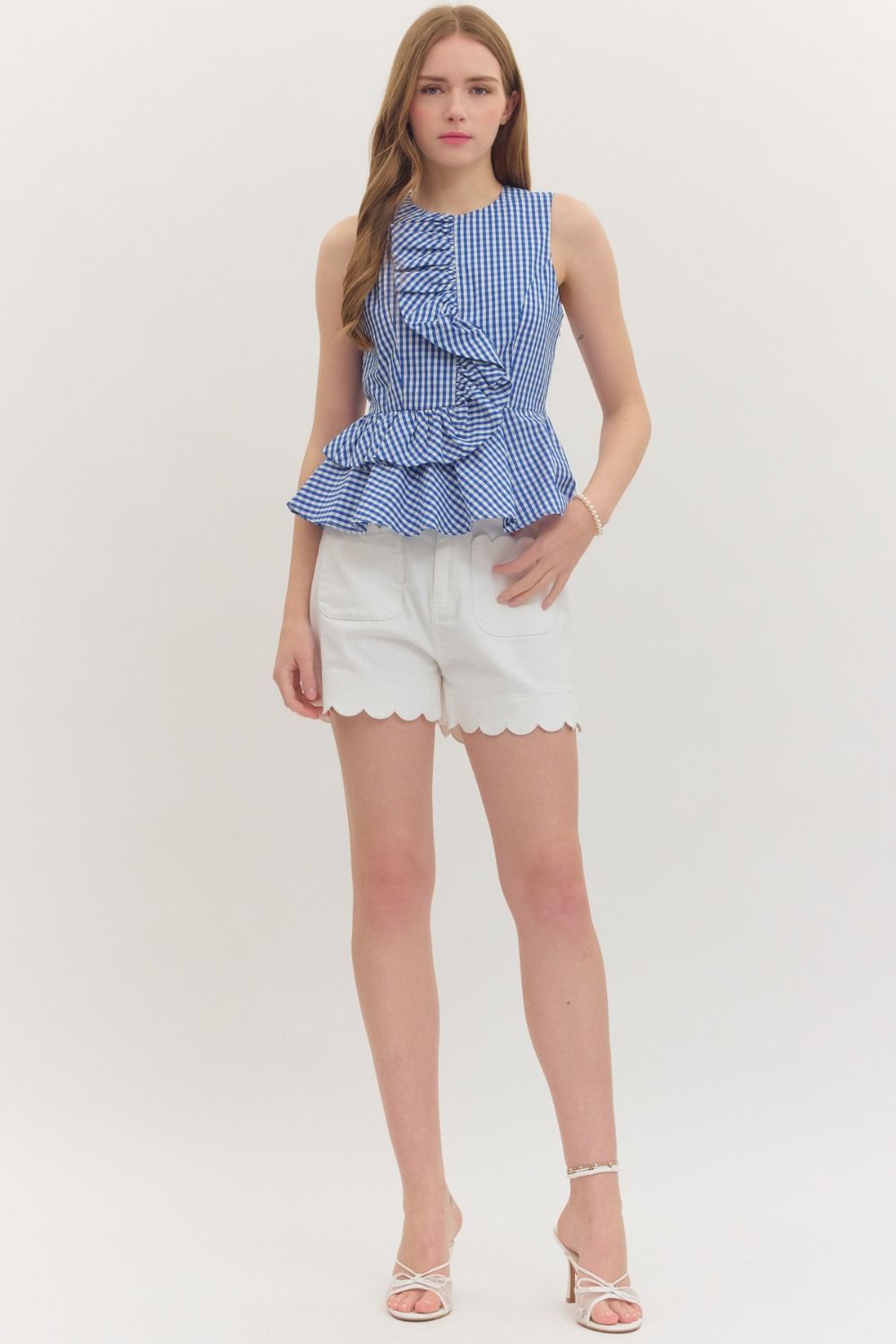 Woman wearing a blue and white Jessica Gingham Sleeveless Peplum Top with asymmetric ruffle detail.