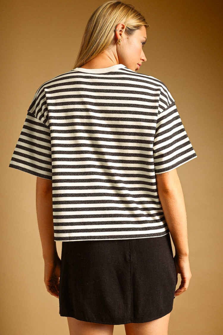 Back view of a woman wearing a black and white bold striped, oversized short sleeve cotton top.