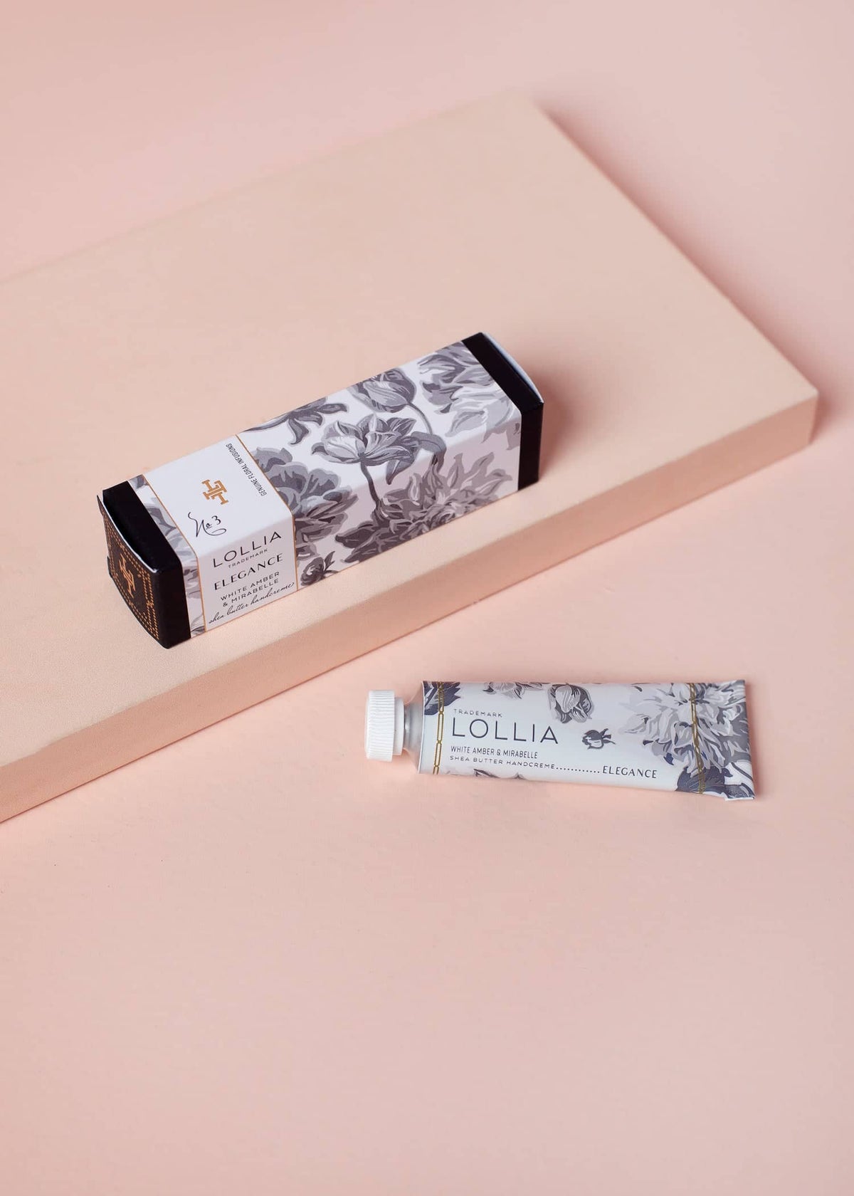 Elegance Petite Treat Handcreme tube and floral patterned box on a light pink surface.