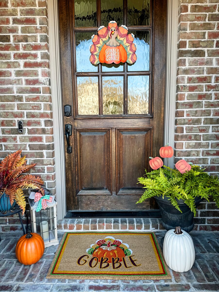 Three small orange pumpkin stakes placed in a green fern planter next to a front door.