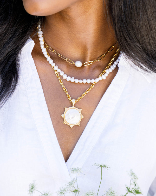 A woman wearing the Penny Necklace, a gold paperclip chain with a central freshwater pearl.