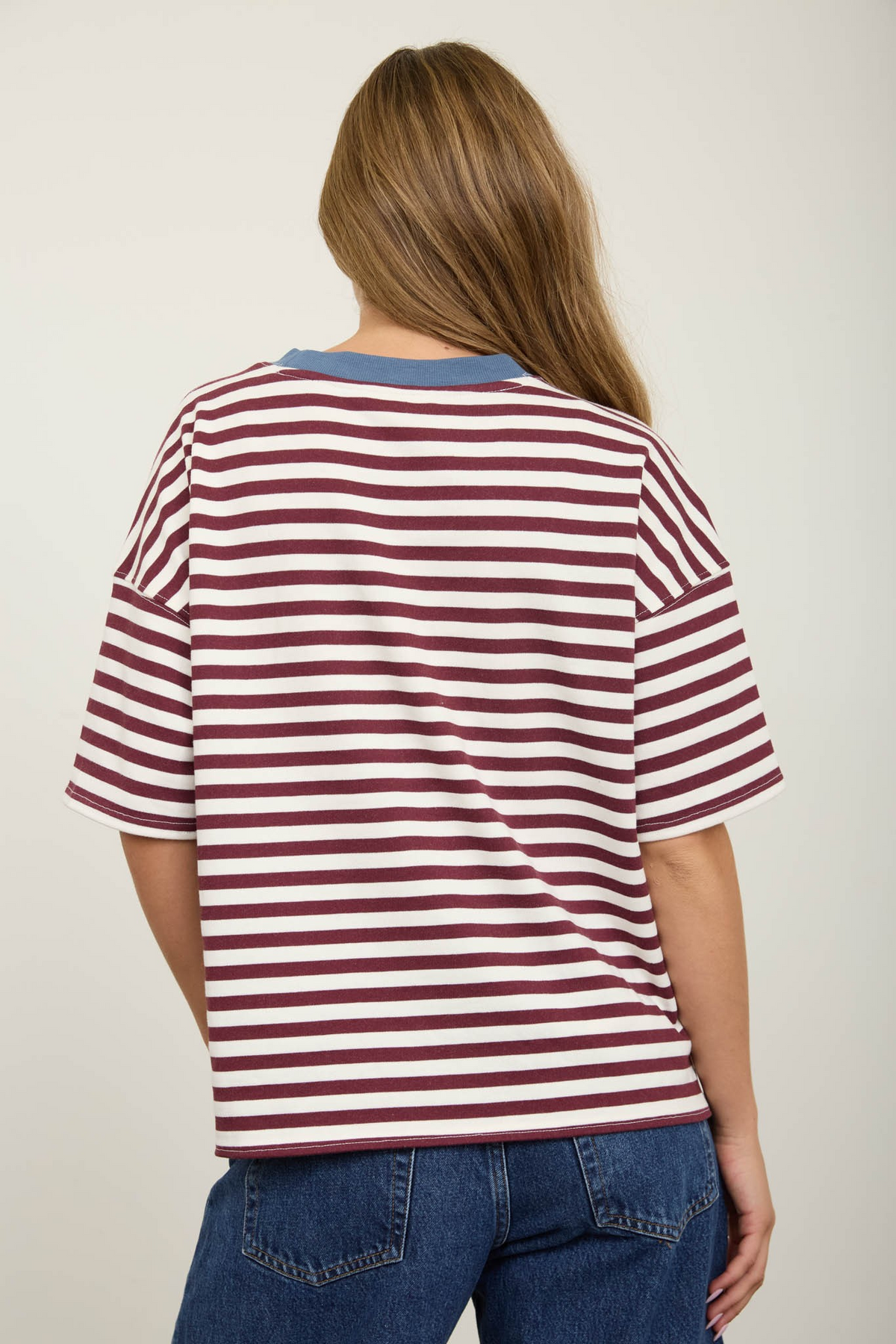 Back view of a woman wearing a burgundy and white striped knit t-shirt with a blue contrast collar.