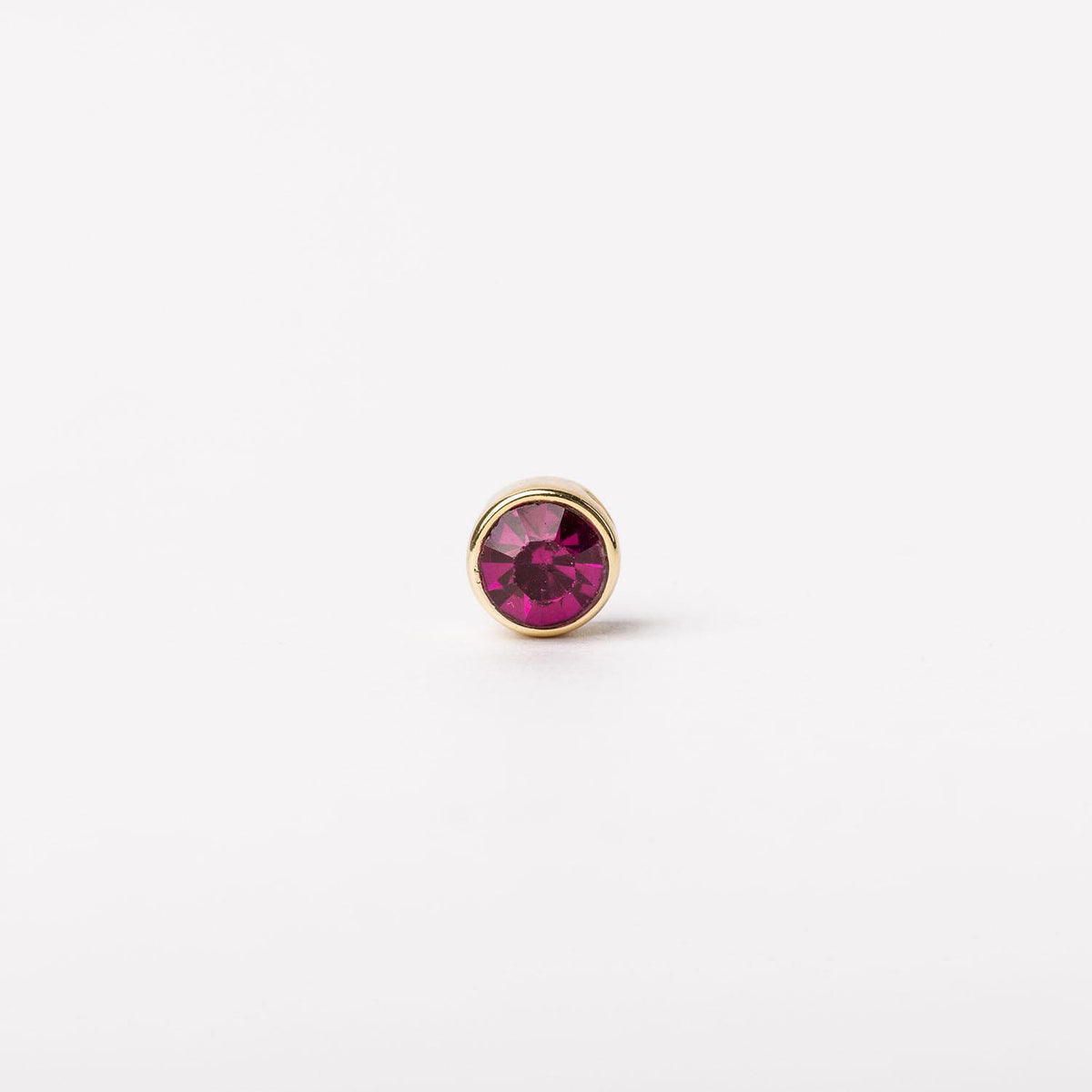 Round gold stud earring featuring a vibrant magenta gemstone in a bezel setting.