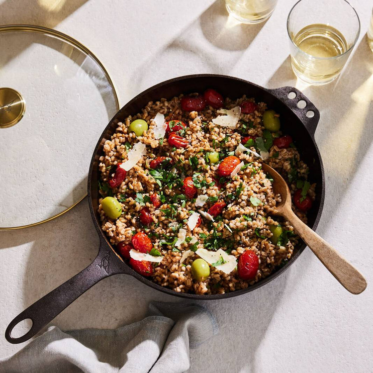 A No. 11 Deep Skillet filled with a grain dish, tomatoes, and olives, next to its glass lid.