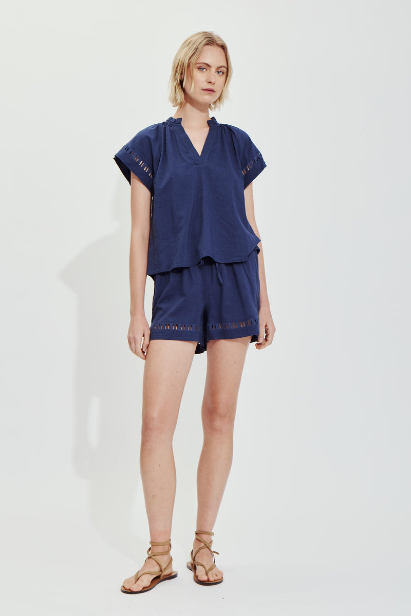Woman wearing navy blue Jasmine shorts with a matching short-sleeve top and tan wrap sandals.