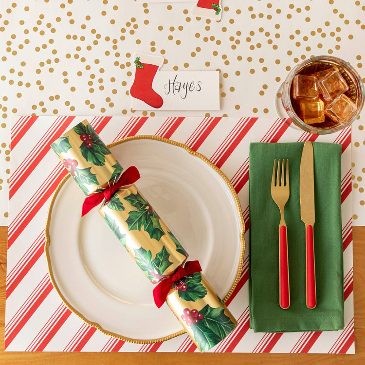 Peppermint Stripe paper placemat with a holiday table setting, gold-rimmed plate, and green napkin.