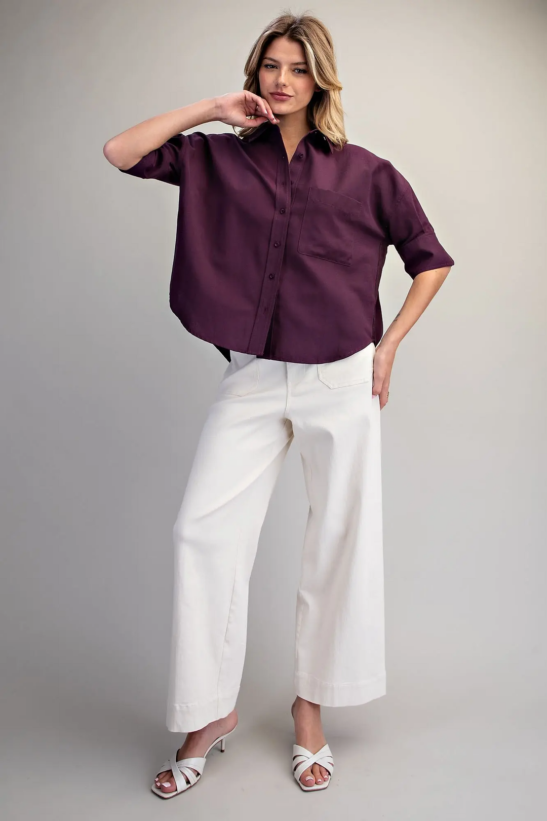 Woman wearing a plum oversized button-up shirt with elbow-length sleeves and white wide-leg pants.