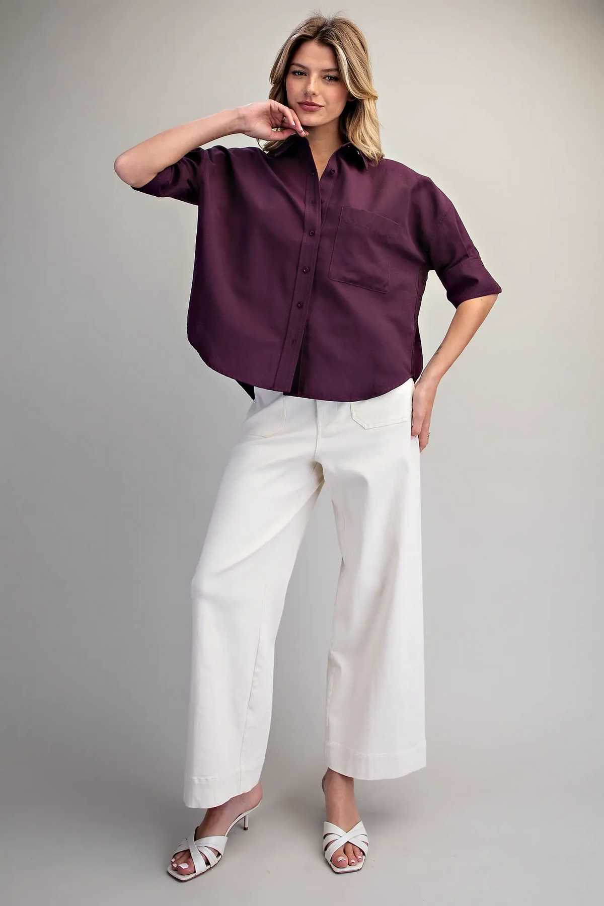 Woman wearing a plum oversized button-up shirt with elbow-length sleeves and white wide-leg pants.