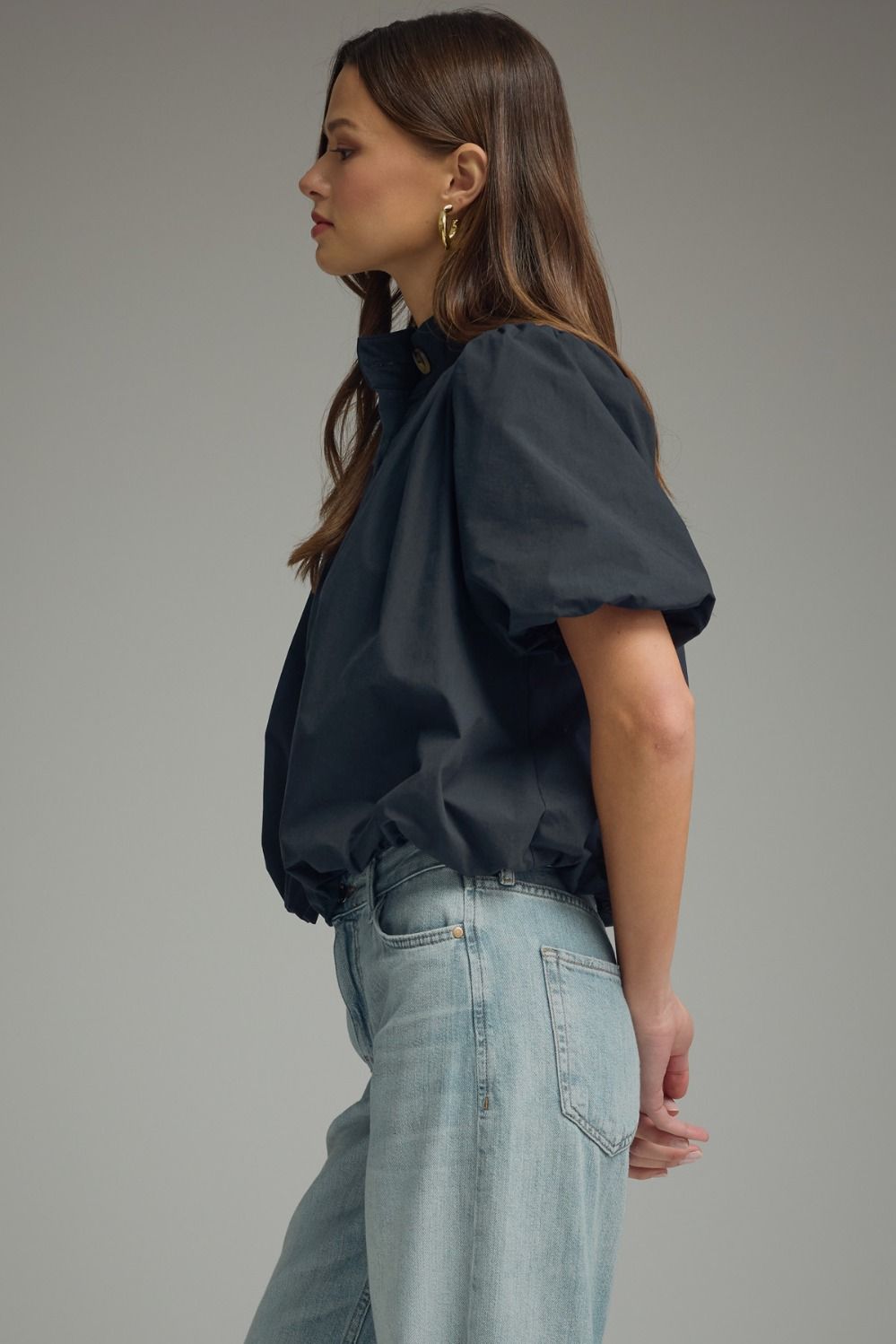 Side view of a woman wearing a navy blue Jacky short puff sleeve top with a bubble hem and jeans.