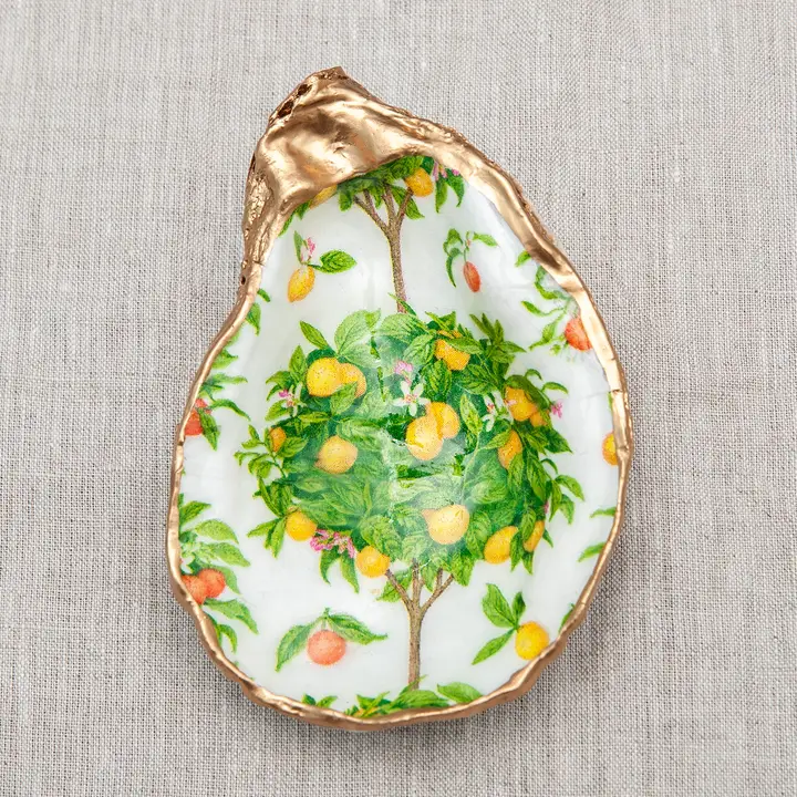 Decoupaged oyster shell with a lemon tree design and metallic gold trim on a linen background.