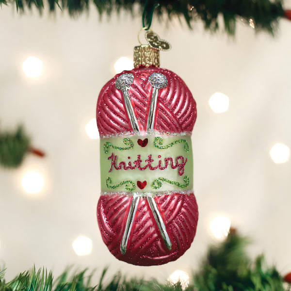 Pink glass yarn skein ornament with silver knitting needles and 'Knitting' text on a green band.