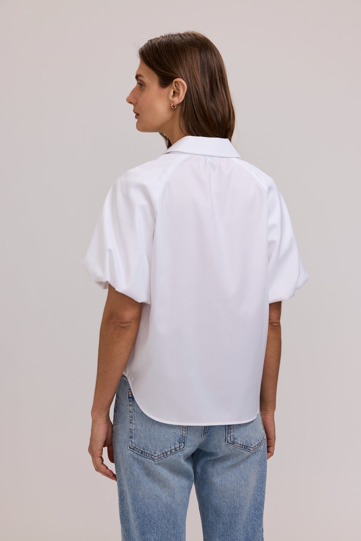 Back view of a woman wearing the white Paula Solid Puff Sleeve Shirt with light wash denim jeans.