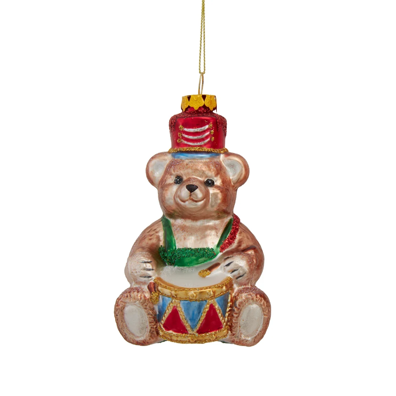 Glass teddy bear ornament wearing a red hat and green scarf, playing a blue and red drum.