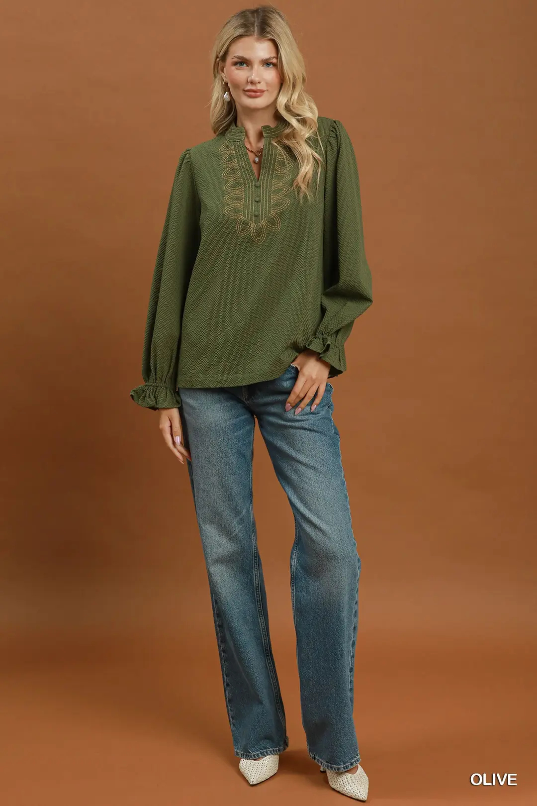 Woman wearing an olive green textured blouse with puff sleeves and embroidery, paired with jeans.