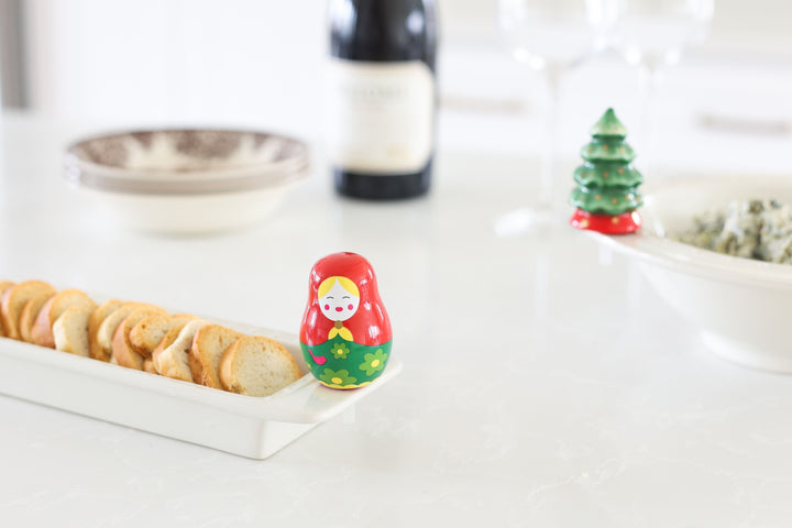 A red and green Russian nesting doll ceramic accessory attached to a white serving tray of bread.