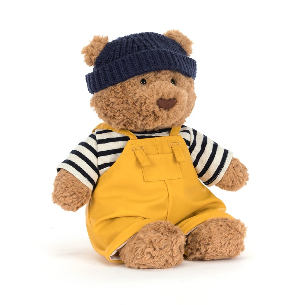 Jellycat Bartholomew Bear in a navy beanie, striped shirt, and yellow overalls.