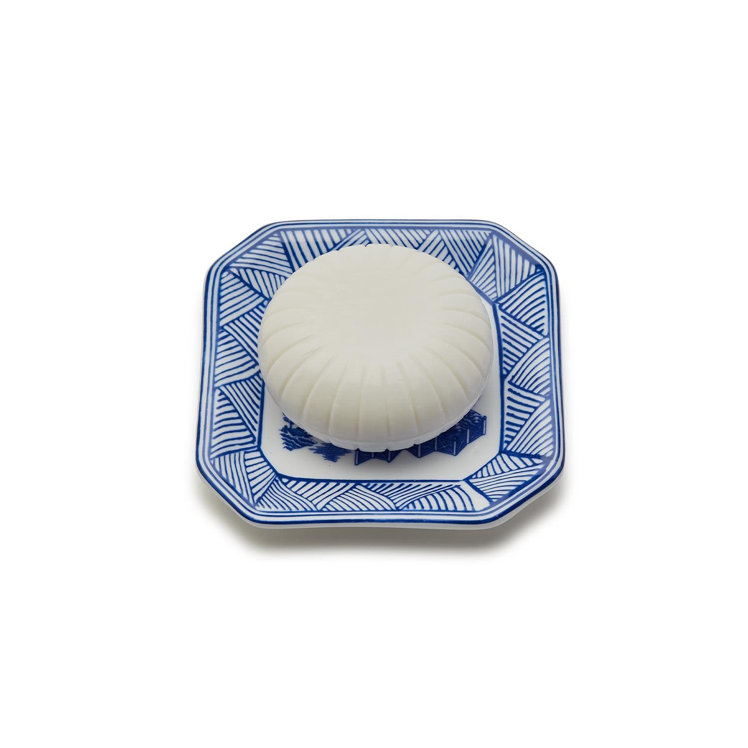 Round white sandalwood soap with embossed ridges on a square blue and white porcelain tray.